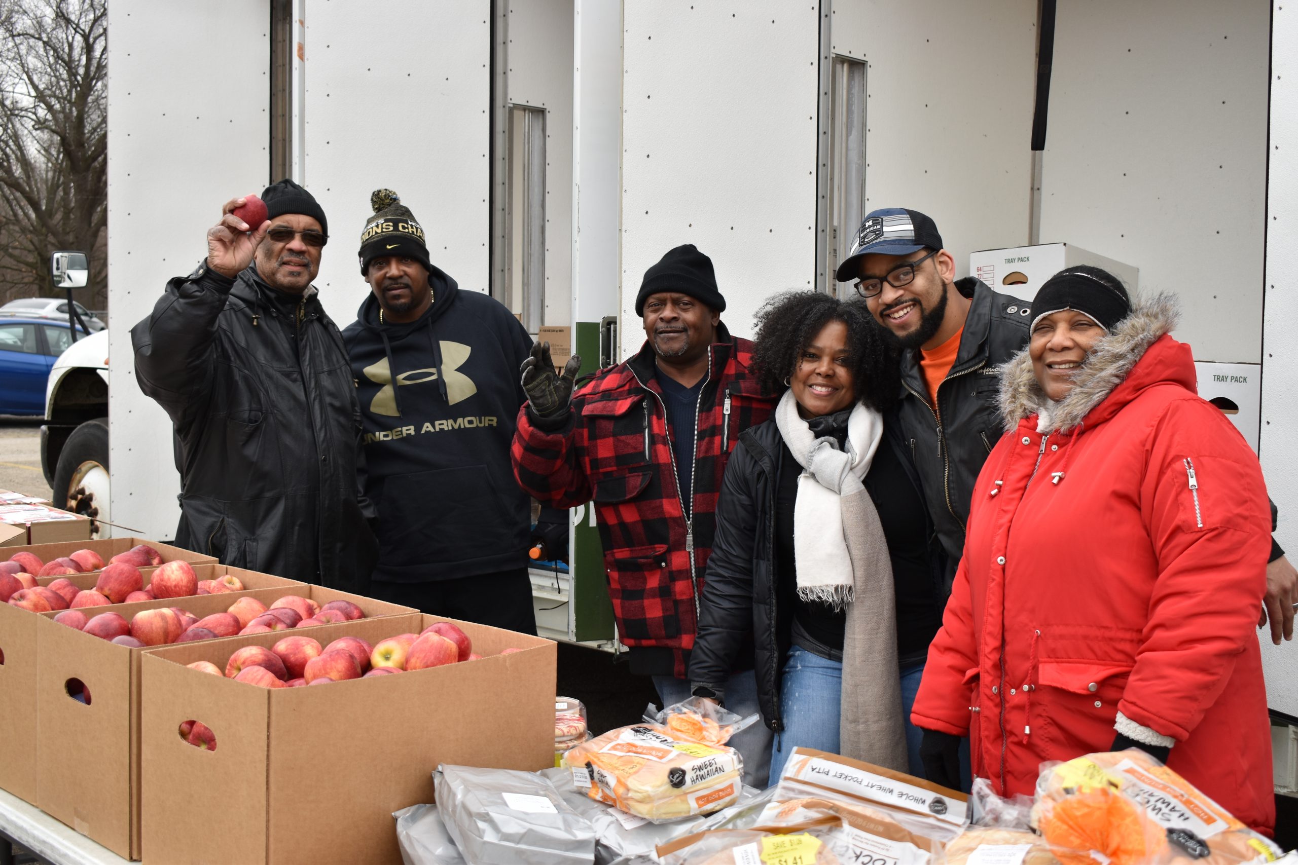 Group of volunteers poses with food and smiles at camera
