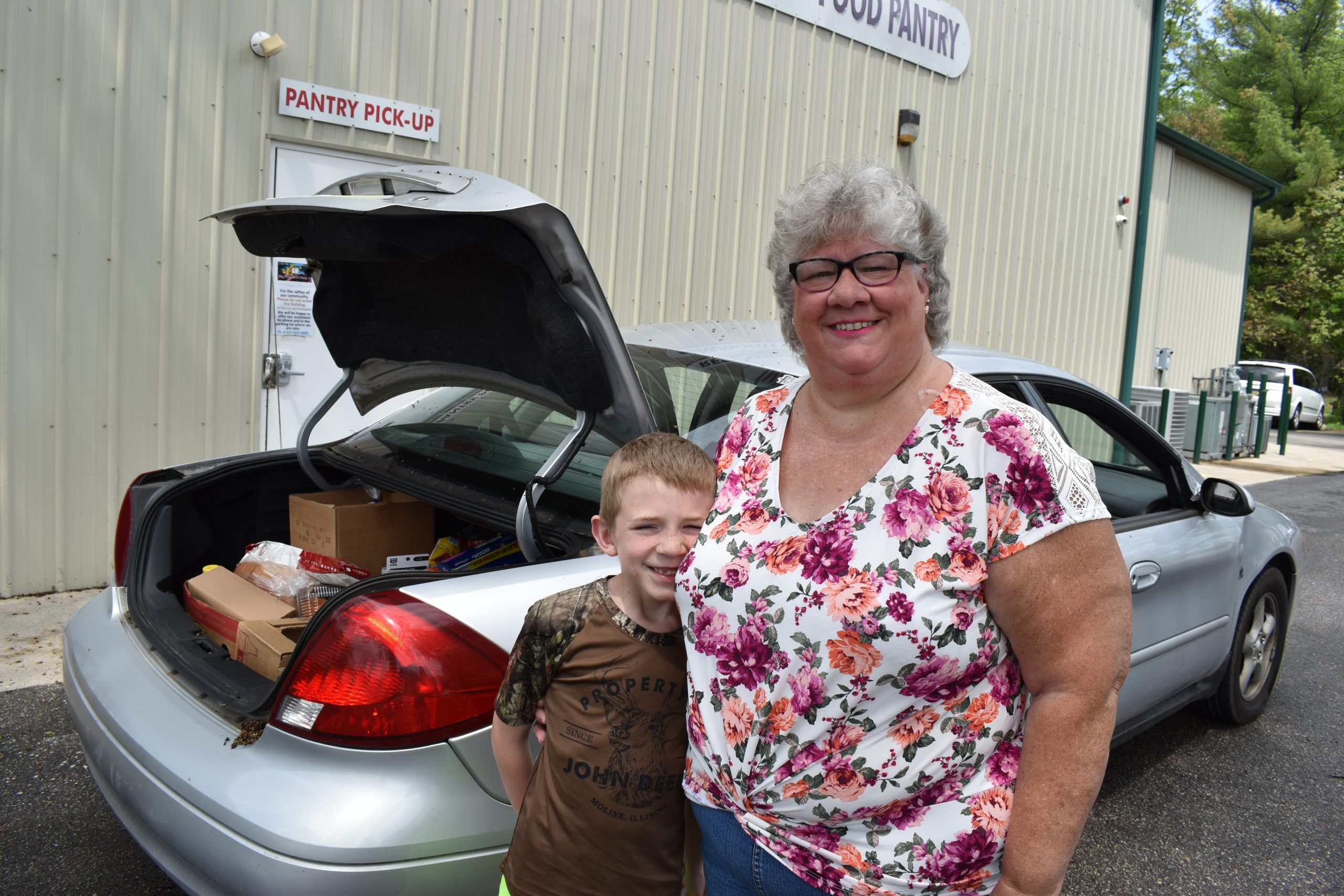 Theresa and her grandson stand in front of their car after receiving food.
