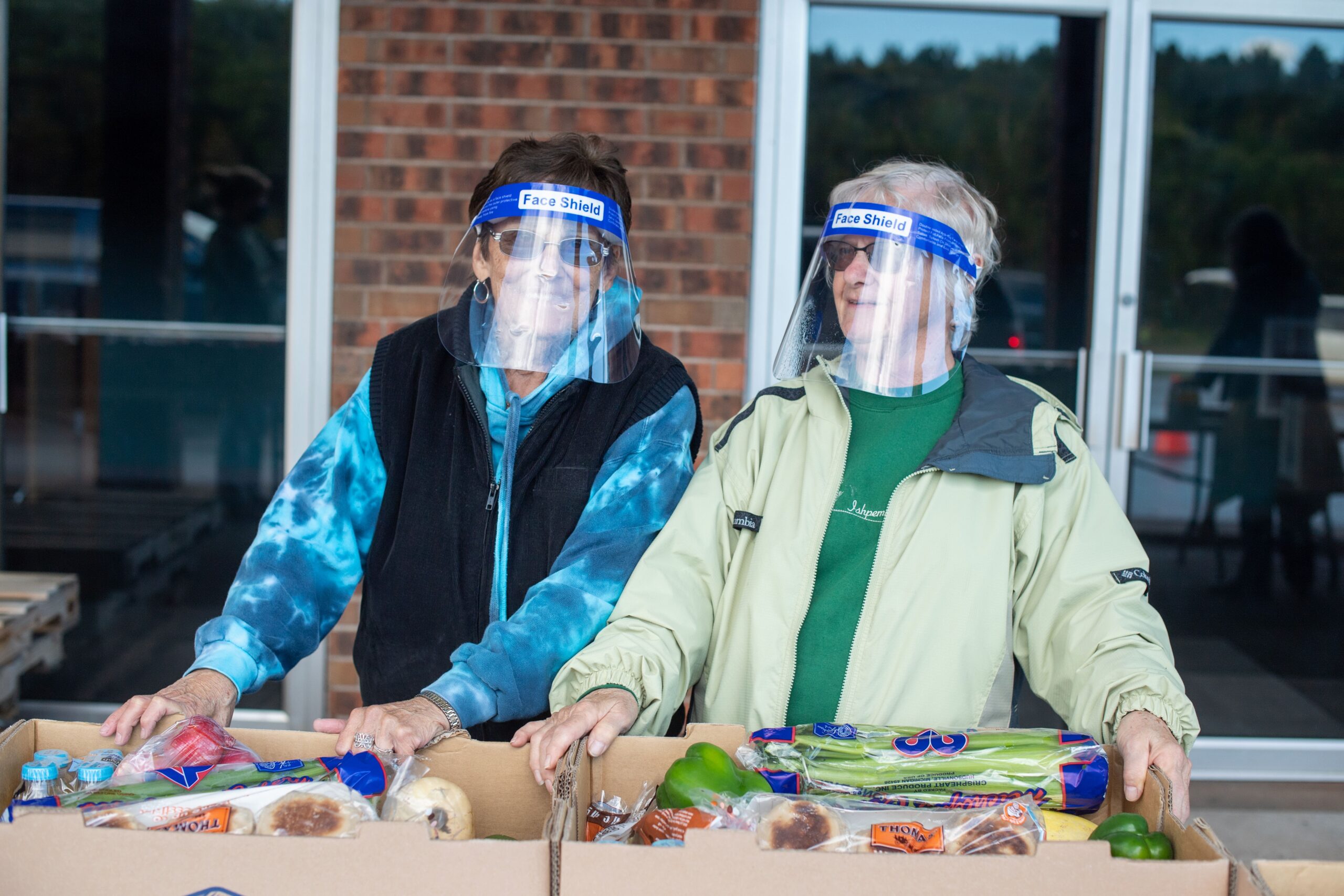 Two women stand behind a row of boxes of food at a Mobile Pantry