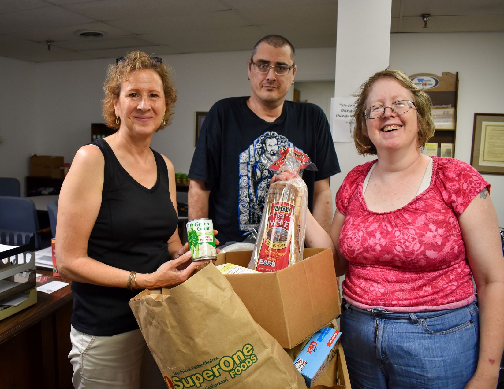 Food pantry volunteer Kathy stands with Yasna and Billy around a cart of food