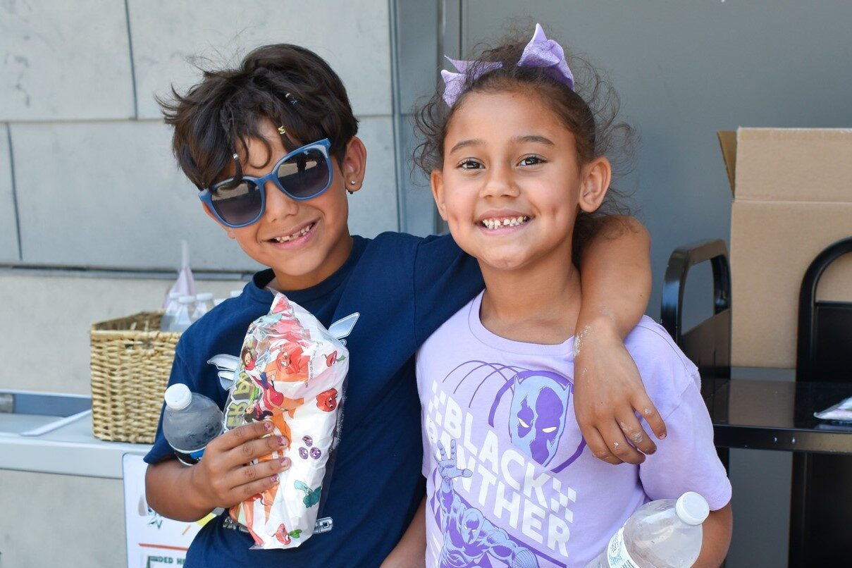 Two children smiling while holding their summer lunch