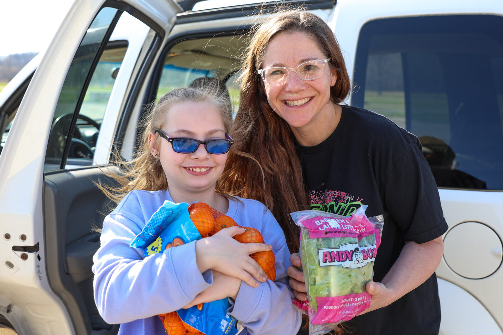 Woman and girl smiling holding up fruits and veggies